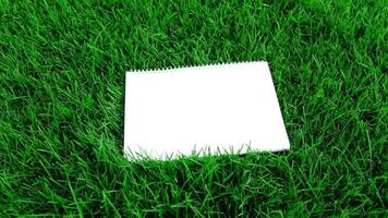 Empty white paper on green grass background. For message flat lay with copy space for text or products presentation. Nature concept, business and lifestyle environment. photo