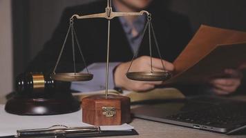 Business and lawyers discussing contract papers with brass scale on desk in office. Law, legal services, advice, justice and law concept picture with film grain effect video