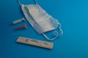 antibody test. a strip for self-diagnosis for coronavirus infection on a blue background. next to the test, a disposable mask, a lancet and a pipette for taking analysis. home test kit photo