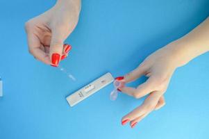 test strip for the determination of coronavirus on a blue background. lab with red manicure dripping solution to detect antibodies. home test to detect the disease photo