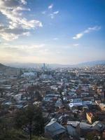 vista vertical desde lo alto de una hermosa ciudad turística con edificios y casas, techos de árboles y plantas, naturaleza contra el cielo azul y montañas. arquitectura antigua europea foto