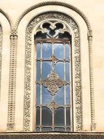 Beautiful vintage ancient old carved window with glass with a forged frame arches and patterns. The background photo