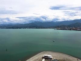 muchos barcos, barcos, cruceros en el puerto y agua en el mar tropical cálido resort de verano con palmeras contra el cielo azul y altas montañas foto