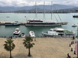 Many ships, boats, cruise liners in the port and water on the tropical sea warm summer resort with palm trees against the blue sky and high mountains photo