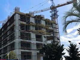 Construction of a monolithic frame house of concrete and gas silicate blocks with a lot of scaffolding using a large crane in a tropical warm resort against the backdrop of palm trees photo