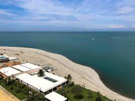 Top view of the sandy beach with sand, sea, green palm trees and buildings, houses on a tropical warm summer resort, rest photo