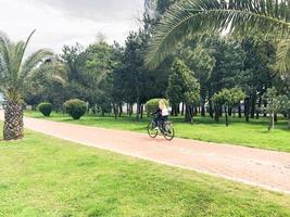 mujer niña montando una bicicleta en el callejón con palmeras verdes en el parque en un cálido resort de verano tropical foto