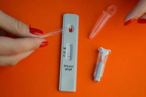 test for coronavirus on an orange background. girl with bright red manicure drips on a drop of blood for the test. nearby is a lancet for a puncture of a finger and a container for saline photo