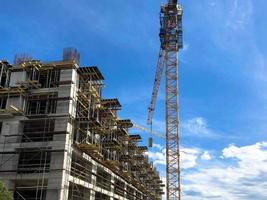 Construction of a monolithic frame house of concrete and gas silicate blocks with lots of scaffolding using a large crane against a blue sky photo