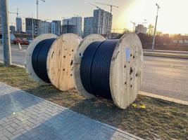 grandes carretes redondos de madera de bobinas con cables, cables eléctricos negros con aislamiento de goma, utilizados en el cableado de líneas conductoras en la construcción industrial foto