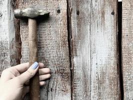 martillo en un mango de madera con un extremo de metal. chica con clavos de martillo de manicura azul en una valla de madera. uñas con estilo, manicura de moda. mujer carpintera foto