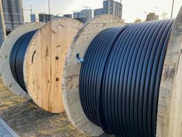 grandes carretes redondos de madera de bobinas con cables, cables eléctricos negros con aislamiento de goma, utilizados en el cableado de líneas conductoras en la construcción industrial foto