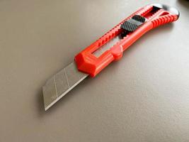 Red sharp office stationery knife with a paper cutting blade on a desktop office desk. Business work photo