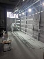 un pintor masculino con un traje protector desechable blanco pinta una estructura metálica con una pistola rociadora en una fábrica de pintura foto