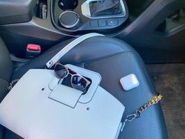 White women's beautiful fashionable leather bag and sunglasses with wireless headphones lie on the leather armchair of a good expensive car photo