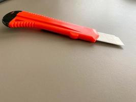 Red sharp office stationery knife with a paper cutting blade on a desktop office desk. Business work photo