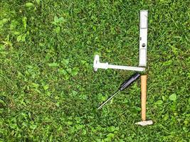 on the grass lies a hammer and a screwdriver, a level and others. K-shaped repair tools are laid out on the lawn. A hammer on a wooden handle, a screwdriver with a black handle photo