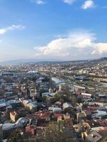 vista vertical desde lo alto de una hermosa ciudad turística con edificios y casas, techos de árboles y plantas, naturaleza contra el cielo azul y montañas. arquitectura antigua europea foto