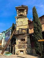 Old stone ancient carved beautiful antique European clock tower with dial on the background of the blue sky and the tourist city. European old architecture photo