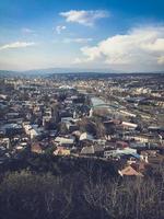 Vertical view from the top from a height of a beautiful tourist city with buildings and houses, roofs of trees and plants, nature against the blue sky and mountains. European old architecture photo