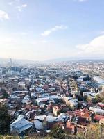 vista vertical desde lo alto de una hermosa ciudad turística con edificios y casas, techos de árboles y plantas, naturaleza contra el cielo azul y montañas. arquitectura antigua europea foto