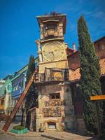 Old stone ancient carved beautiful antique European clock tower with dial on the background of the blue sky and the tourist city. European old architecture photo