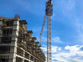 Construction of a monolithic frame house of concrete and gas silicate blocks with lots of scaffolding using a large crane against a blue sky photo