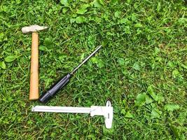 hay un martillo y un destornillador en la hierba, nivelados. las herramientas de reparación se extienden sobre el césped en forma de un programa creciente. martillo con mango de madera, destornillador con mango negro foto