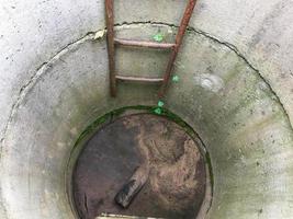 homemade well. concrete rings are installed in the courtyard of the house to extract resources from the ground. moss grows inside and there is a rusty staircase. abandoned well photo