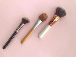 hermosos pinceles y pinceles blancos y dorados cosméticos de belleza a la moda para aplicar maquillaje y polvo y cosméticos en la cara sobre un fondo rosa suave. endecha plana foto