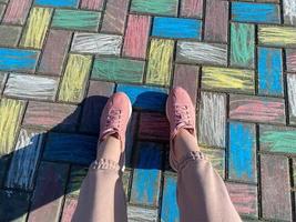 hermosas piernas femeninas con zapatillas rosas y pantalones de moda sobre un fondo de losas de hormigón pintadas con alegres crayones coloridos para niños foto