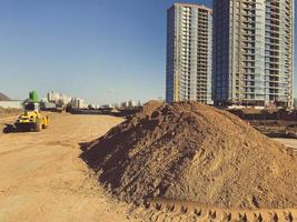 A large pile of yellow sand for the repair and construction of tall new buildings and structures of houses. New construction machinery and equipment at the construction site photo