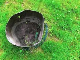 el cubo está en la hierba. un balde para residuos, agricultura, manchado de aceite combustible negro. balde sobre un fondo de flores, en el fondo de la tierra para macizos de flores foto