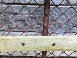 texture, metal mesh. on the net there are wooden sticks nailed down. homemade fence. rusty mesh with damage, corrosion and rust. the boards are nailed down with rusty old nails photo