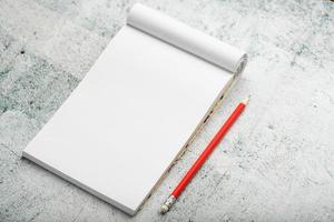 Notepad with red pencil on white plastered wall background, for education, write goals and deeds photo