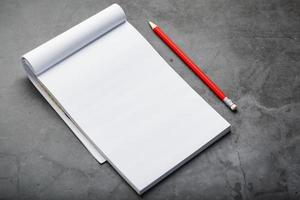 Notepad with a red pencil on a black stone plate background, for education, recording goals and deeds photo