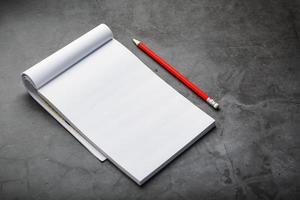 Notepad with a red pencil on a black stone plate background, for education, recording goals and deeds photo