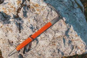 An ice ax with a wooden orange handle lies on a gray stone. Traveling photo