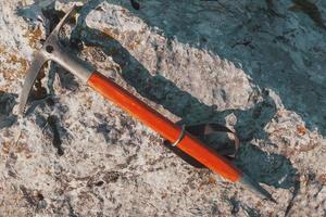 An ice ax with a wooden orange handle lies on a gray stone. Traveling photo