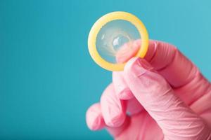anticoncepción del condón una mano en un guante rosa sostiene un condón sobre un fondo azul. látex para semen y protección contra el embarazo. foto
