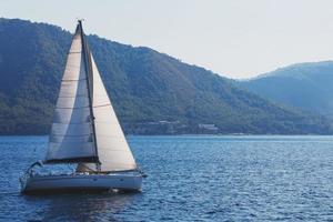 Sailing yacht with white sails on a wavy sea bay on a background of mountains. photo