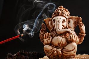 dios hindú ganesh sobre un fondo negro. estatua de rudraksha y rosario sobre una mesa de madera con un palo de incienso rojo y humo de incienso foto