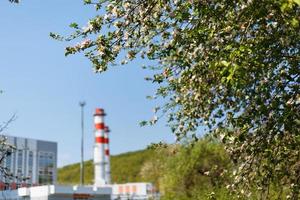 planta de energía de turbina de gas de gas natural con chimeneas de color rojo-blanco contra el cielo azul en el huerto de manzanas foto