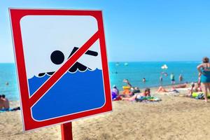una señal en la playa no está permitida para nadar, la gente se baña y descansa en el mar a pesar de la señal y la prohibición. foto