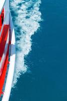 The red side of the cruise ship cuts through the blue sea surface, leaving the waves photo