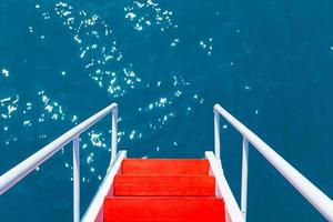 The red staircase with white railings goes into the azure clear waters of the Black Sea photo