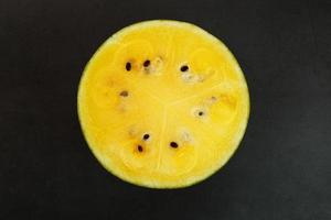 Half of tasty and ripe yellow watermelon on a black background, texture of juicy pulp of ripe yellow watermelon with seeds photo