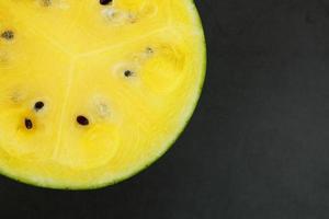 Half of tasty and ripe yellow watermelon on a black background, texture of juicy pulp of ripe yellow watermelon with seeds photo