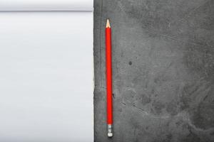 bloc de notas con un lápiz rojo sobre un fondo de placa de piedra negra, para educación, registro de objetivos y hechos foto