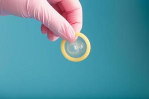 un condón abierto en una mano con un guante rosa se sostiene sobre un fondo azul. látex para la protección contra el embarazo. foto